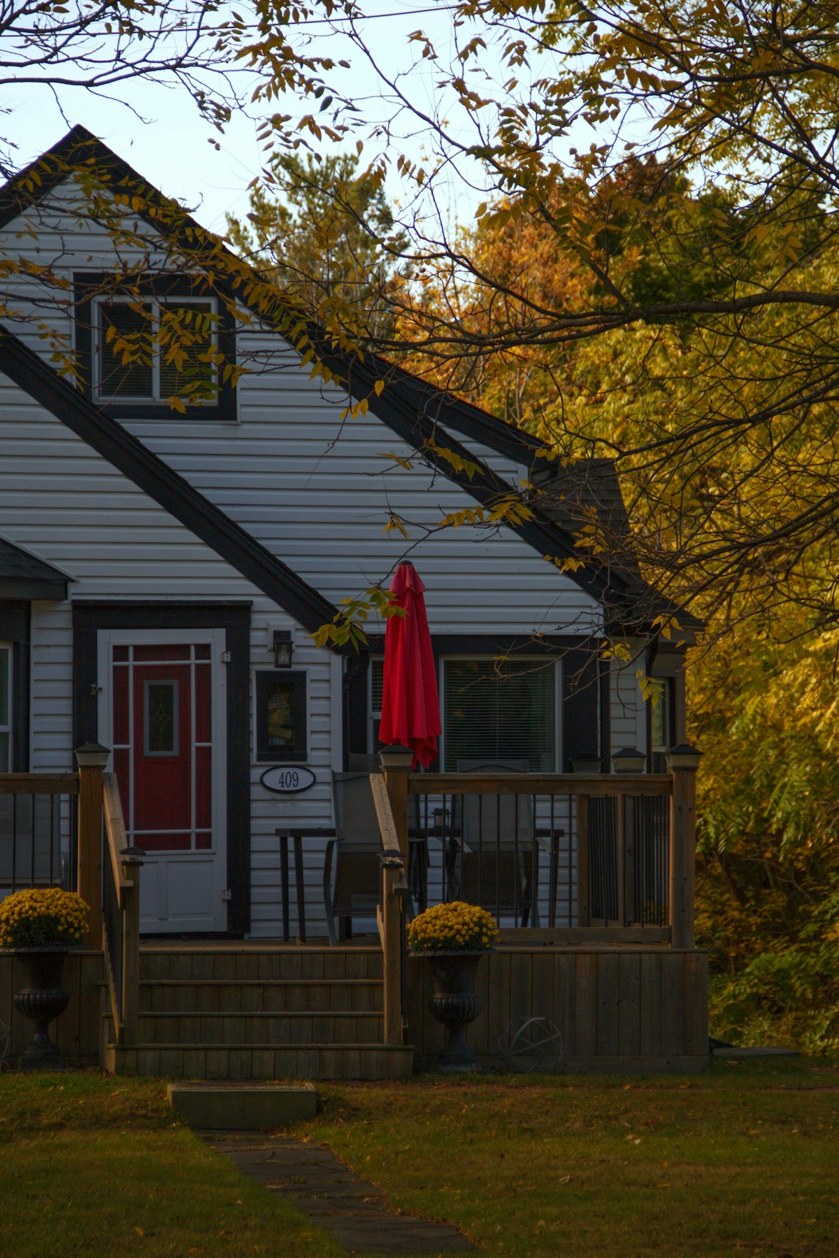 A white house with a red front door among autumn trees.