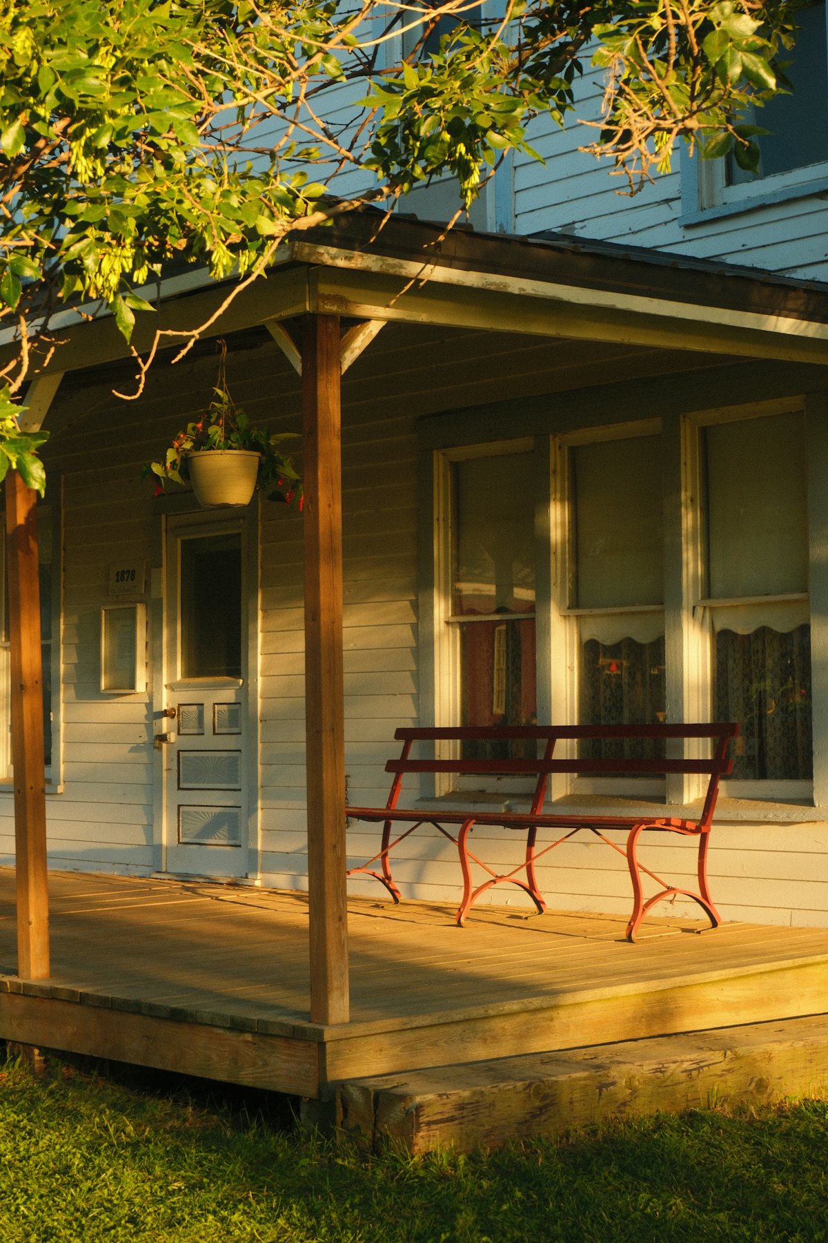 A wooden front porch with a red bench, lit by low evening sun.